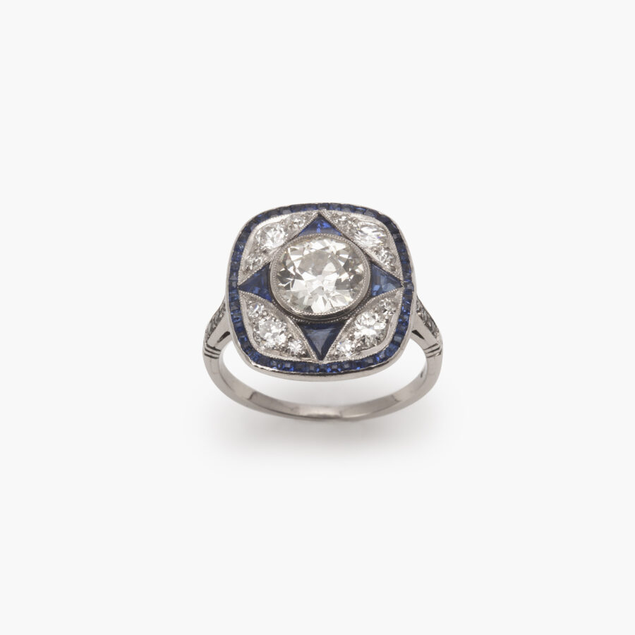 A platinum Art Deco ring, set with antique brilliant cut diamonds and calibrated blue sapphires in a geometrical design, made ca 1920.