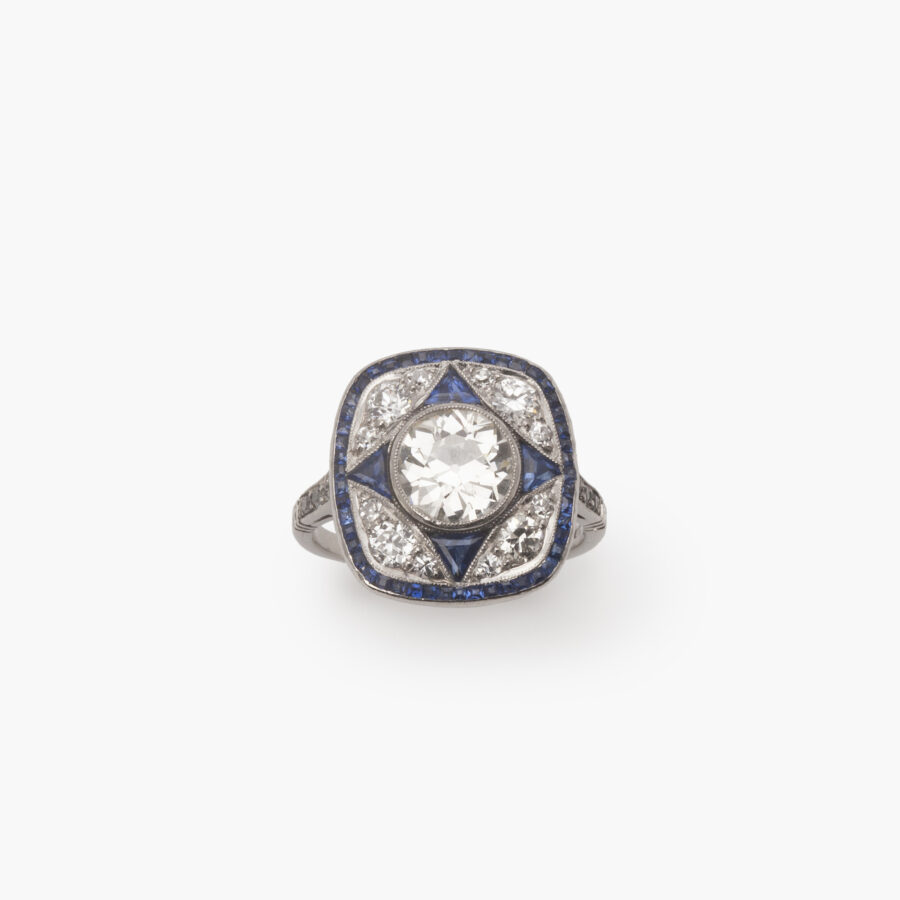 A platinum Art Deco ring, set with antique brilliant cut diamonds and calibrated blue sapphires in a geometrical design, made ca 1920.