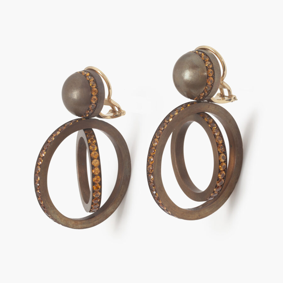 A pair of eighteen carat white gold and satiné copper earrings, set with round facetted orange garnets. Signed Hemmerle, made in Munich, early 21st century.