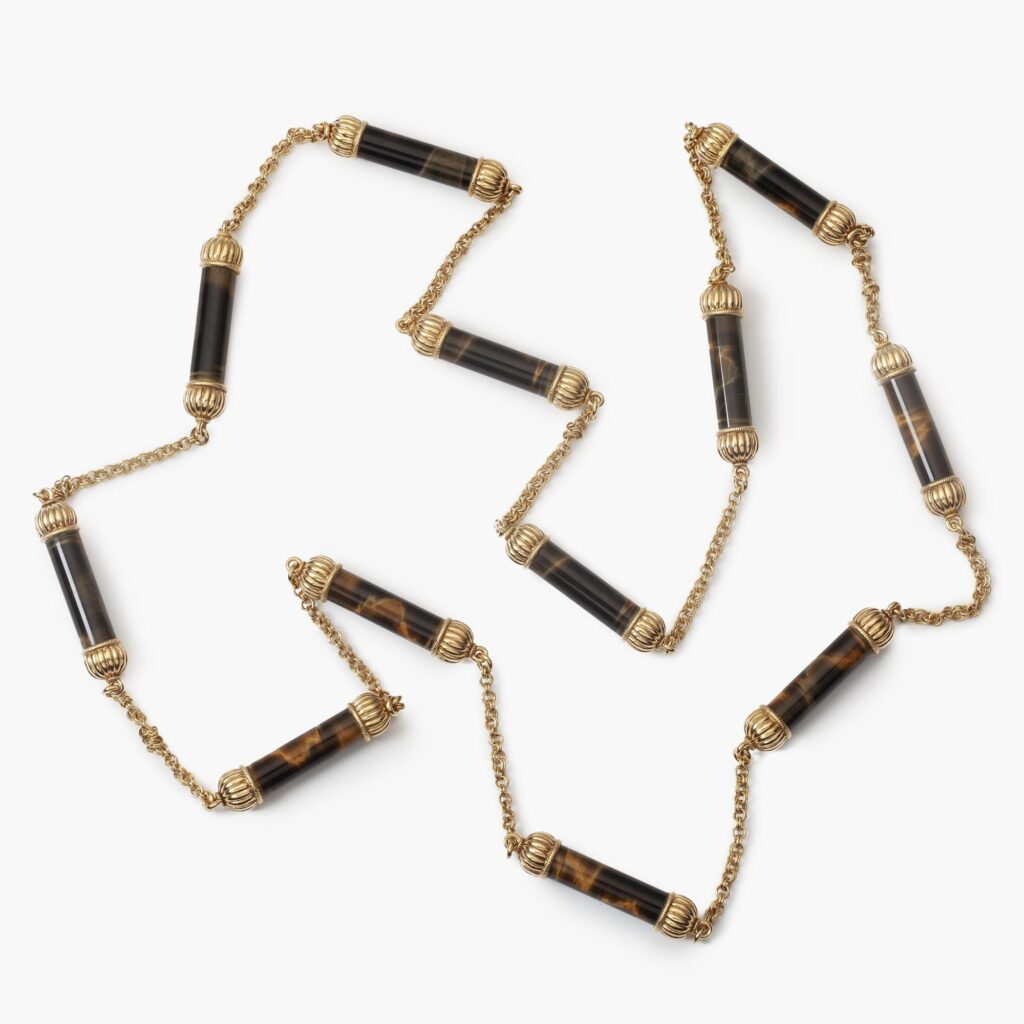 An eighteen carat yellow gold longchain comprising twelve bars of tiger’s/falcon’s eye connected by double ancre chain. Georges Lenfant, Paris, ca 1970.